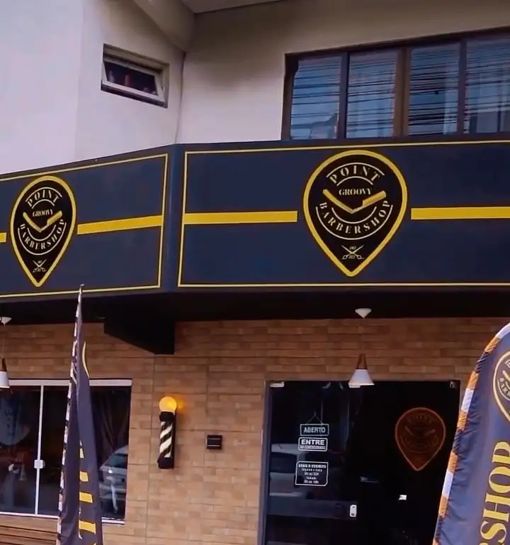 Fachada da Point Groovy: letreiro preto com faixa amarela e o logo, parede de tijolo e poste de barbeiro